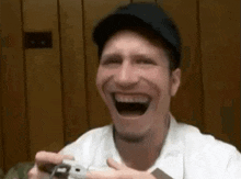 a man is laughing while holding a video game controller in his hands .