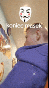 a man in a blue jacket is standing in a hallway with a mask on his face and the words koniec masek above him