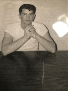 a man in a white shirt is sitting at a table with his hands folded