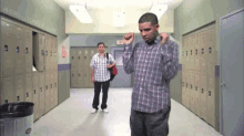 a man in a plaid shirt is dancing in a hallway with lockers and a trash can in the foreground