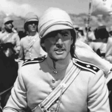 a black and white photo of a man in a military uniform with a hat on his head .