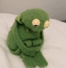 a green stuffed frog is sitting on a bed with its eyes closed .