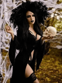 a woman dressed as a witch is holding a skull in her hand .