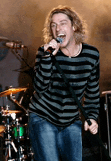 a man singing into a microphone while wearing a striped shirt and jeans