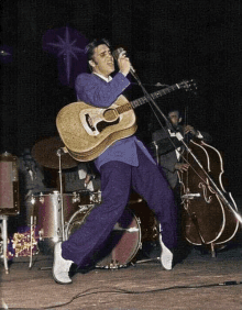 elvis presley is singing into a microphone while playing an acoustic guitar on stage .