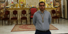 a man wearing glasses and a medal around his neck stands in front of a chair