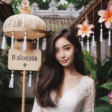 a woman in a white dress stands in front of a sign that reads balon168