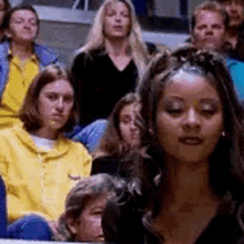 a group of people are sitting in a stadium watching a game and one woman is looking at the camera .