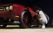 a man squatting next to a red car with the word srt on the side