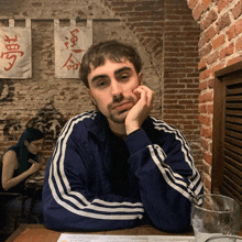 a man sitting at a table with his hand on his chin in front of a brick wall