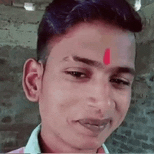 a young man with a red circle on his forehead is smiling for the camera .