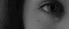 it is a black and white photo of a woman 's eye with a tear coming out of it .