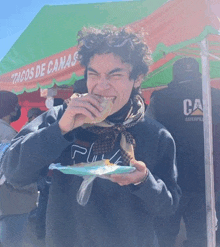 a man is eating a sandwich under a tacos de canas tent