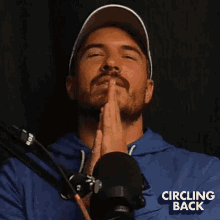 a man is clapping his hands in front of a microphone while wearing a blue shirt that says circling back