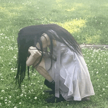 a woman with long black hair is kneeling in a field