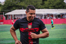 a man wearing a black shirt with a red cross on it is running on a field