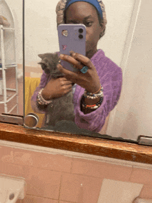 a woman taking a picture of herself holding a cat in front of a mirror