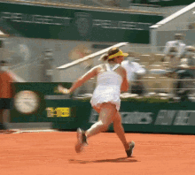 a woman in a white dress is running on a tennis court in front of a sign that says peugeot