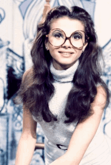 a woman wearing glasses and a turtleneck smiles