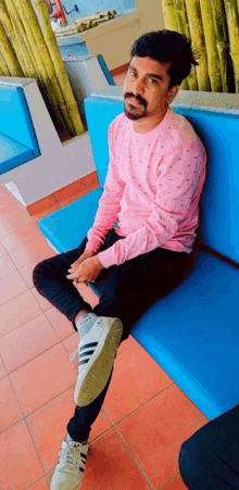 a man in a pink shirt sits on a blue bench with his legs crossed