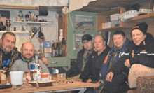 a group of men sitting around a table with one wearing a black hat that says ' a '