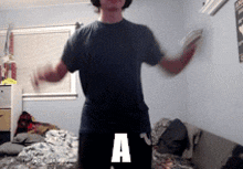 a man in a black shirt is standing in front of a bed with the letter a on his pants