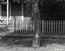 a black and white photo of a house with a wooden fence and the words $ dood on the bottom right