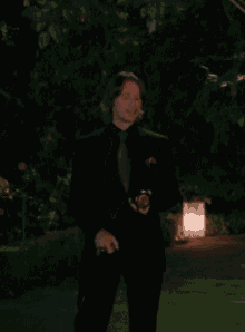 a man in a black suit is standing in a dark garden