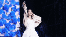 a woman in a white dress is singing into a microphone on stage