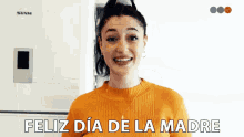 a woman in an orange sweater says feliz dia de la madre in spanish