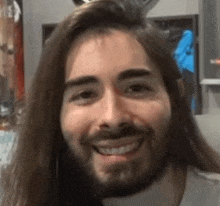 a man with long hair and a beard is smiling in a room .