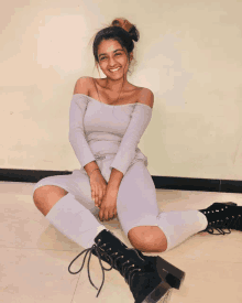 a woman sits on the floor wearing a grey off the shoulder top