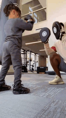 a man and a child wearing boxing gloves and pads in a gym