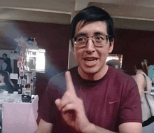 a man wearing glasses and a maroon nike shirt holds up his finger