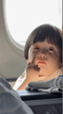 a little boy is sitting on a plane looking out the window .