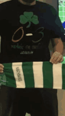 a man wearing a black shirt with a shamrock on it is holding a green and white scarf