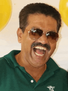 a man wearing sunglasses and a green shirt is laughing with his mouth open