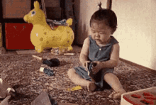 a baby is sitting on the floor playing with toys and a yellow rocking horse is in the background .