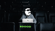 a man wearing sunglasses is sitting in a dark auditorium with a laptop and the word $ dood on the seat