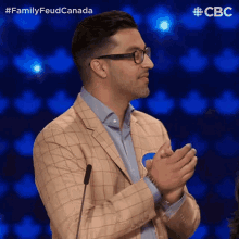 a man in a suit and glasses applauds in front of a microphone with a cbc logo in the background