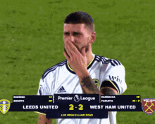 a soccer player covering his mouth with his hand in front of a scoreboard that says premier league 2 2 west ham united