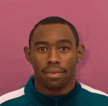 a close up of a man 's face with a pink background and a green jacket on .