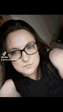 a woman wearing glasses and a black tank top has a tiktok watermark on her face