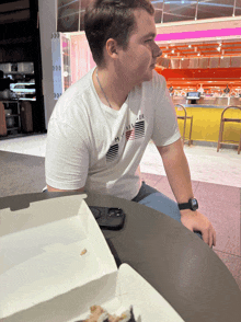 a man sits at a table with a box of food in front of him and a t-shirt that has the word miller on it