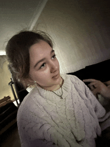 a girl wearing a white sweater and a necklace looks to the side