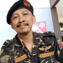 a man with a beard wearing a black beret and a camouflage uniform is smiling for the camera .