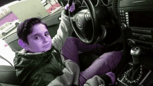 a young boy is sitting in the driver 's seat of a car with purple eyes .