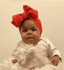 a baby wearing a red headband and a white dress looks at the camera