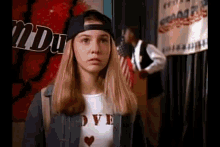 a young girl wearing a baseball cap and a t-shirt with the word love on it is standing in front of an american flag .