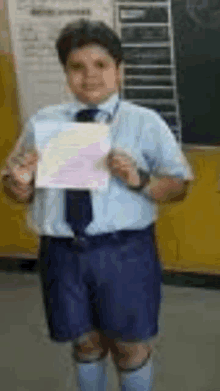 a young boy in a blue shirt and tie is holding a piece of paper in a classroom .